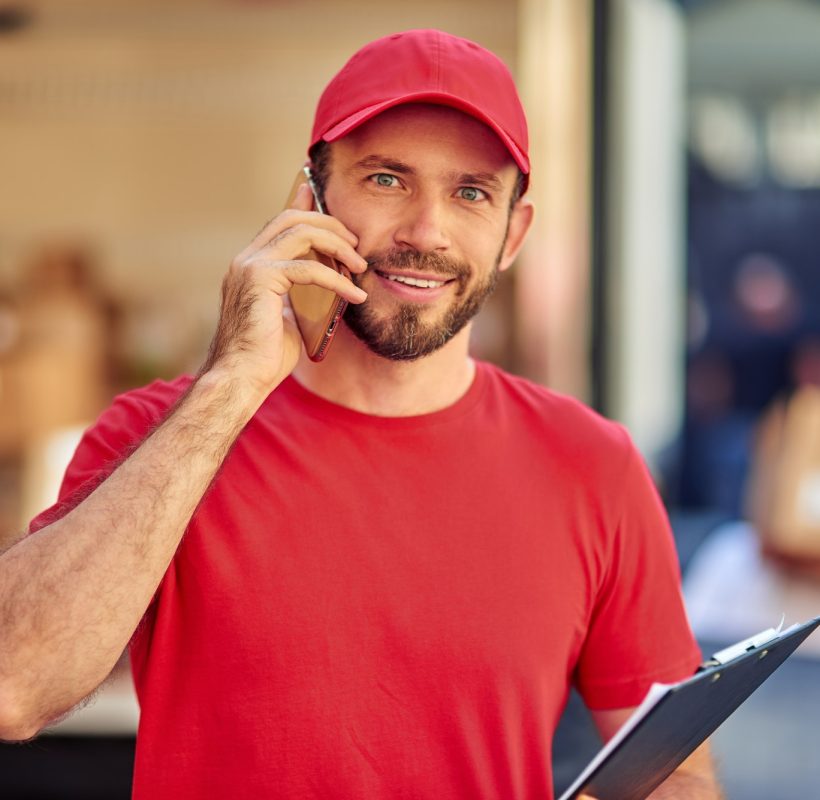 young-cheerful-caucasian-male-courier-in-red-uniform-talking-on-phone.jpg